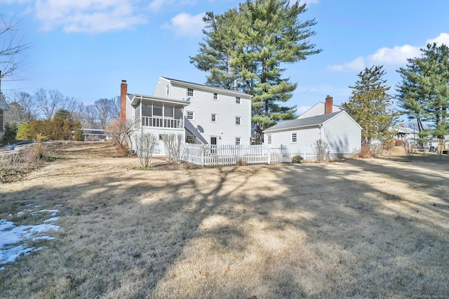 back of house with a yard, a sunroom, fence, and a chimney