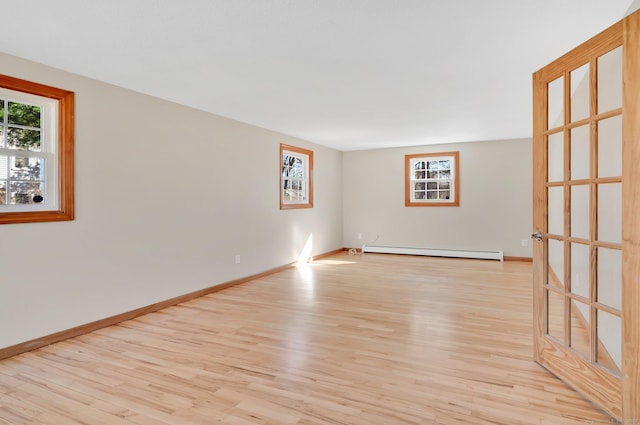 empty room featuring a baseboard heating unit, light wood-type flooring, and plenty of natural light