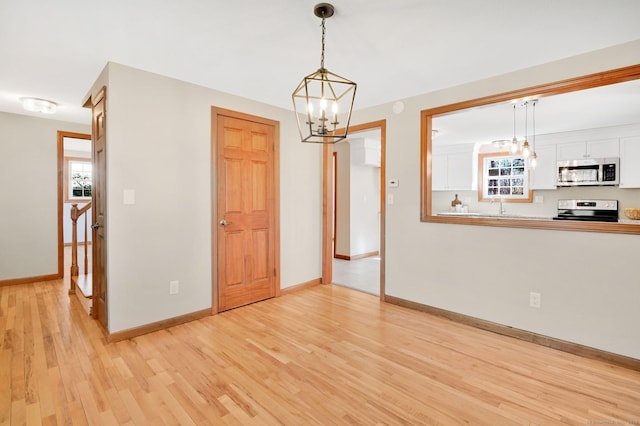 interior space with light wood-style floors, a sink, baseboards, and an inviting chandelier