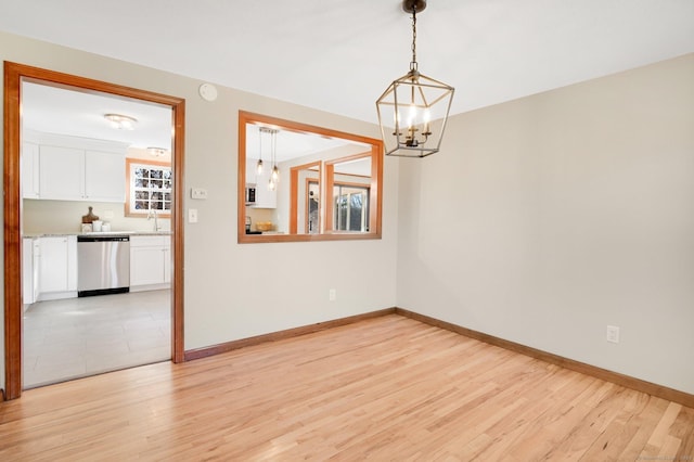 unfurnished room with a chandelier, light wood-type flooring, and baseboards