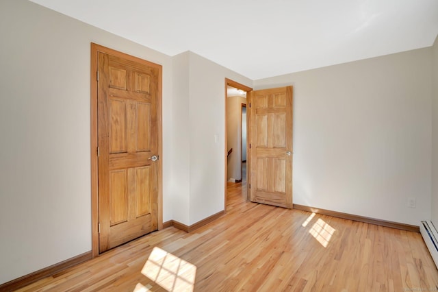 unfurnished bedroom with light wood-style floors, a baseboard radiator, and baseboards