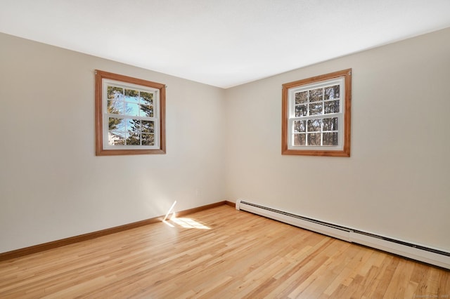 empty room with light wood-style floors, a baseboard heating unit, and a wealth of natural light