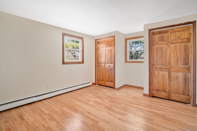 unfurnished bedroom featuring two closets, light wood-style flooring, a baseboard heating unit, and baseboards