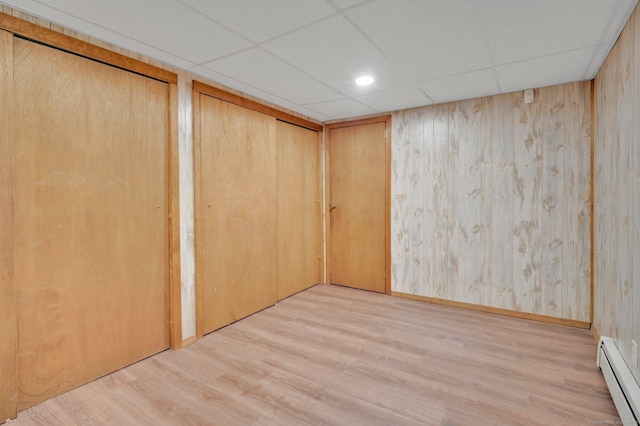 interior space featuring a baseboard heating unit, a drop ceiling, baseboards, and wood finished floors