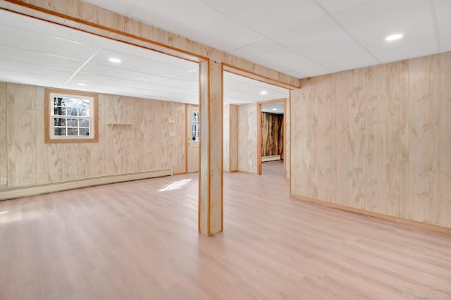 basement with a paneled ceiling, wooden walls, baseboard heating, and wood finished floors