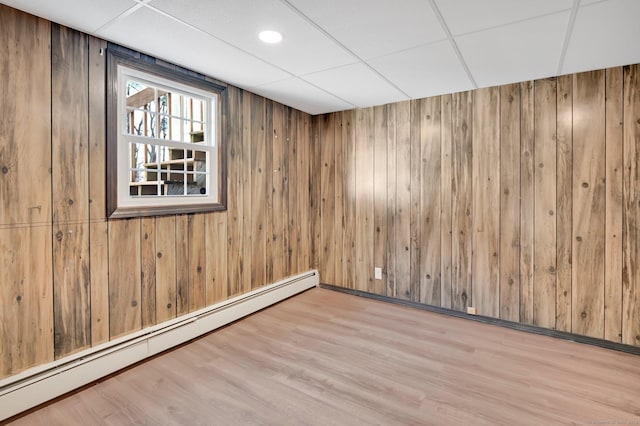 spare room featuring a baseboard radiator, wood finished floors, a paneled ceiling, and wooden walls