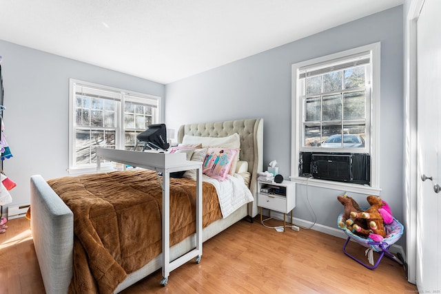 bedroom featuring light wood-type flooring, multiple windows, a baseboard heating unit, and cooling unit