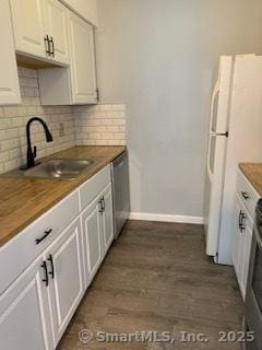 kitchen featuring tasteful backsplash, freestanding refrigerator, stainless steel dishwasher, wooden counters, and a sink