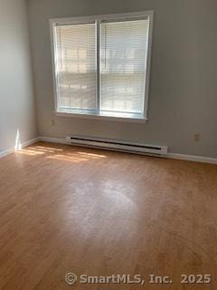 empty room featuring baseboard heating, wood finished floors, and baseboards