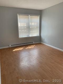 spare room featuring baseboards, a baseboard heating unit, and wood finished floors