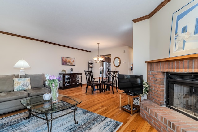 living area featuring a fireplace, an inviting chandelier, light wood-style floors, and ornamental molding