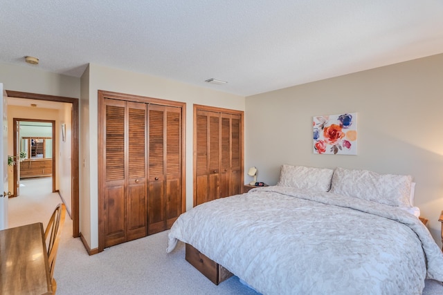 bedroom featuring light carpet, visible vents, a textured ceiling, and two closets