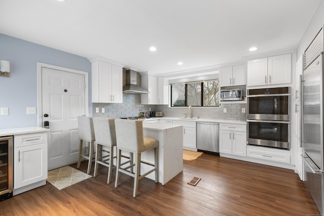 kitchen featuring a sink, white cabinets, appliances with stainless steel finishes, wall chimney range hood, and dark wood finished floors