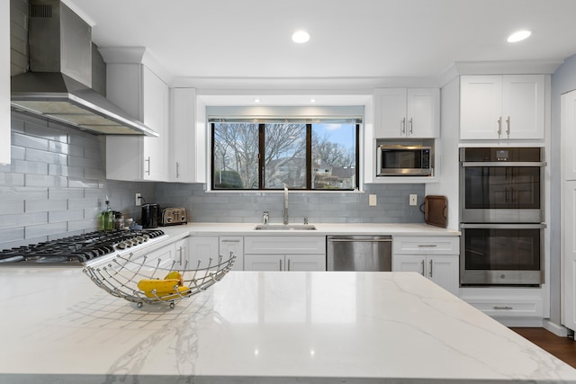 kitchen with white cabinets, wall chimney exhaust hood, appliances with stainless steel finishes, a sink, and backsplash