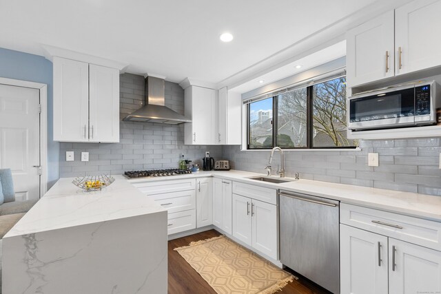 kitchen featuring stainless steel appliances, dark wood-style flooring, a sink, white cabinetry, and wall chimney range hood