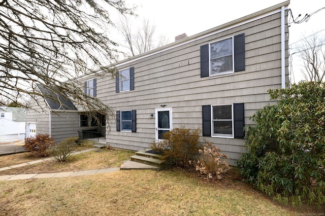 back of house featuring a chimney and a lawn