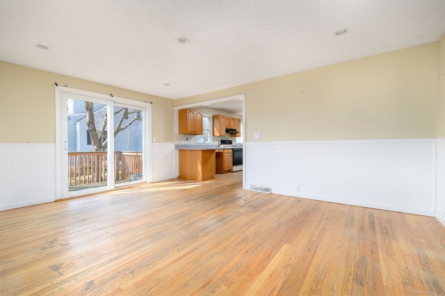 unfurnished living room with light wood-style flooring, wainscoting, and visible vents