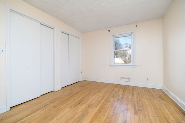 unfurnished bedroom featuring a textured ceiling, two closets, light wood-style flooring, and baseboards