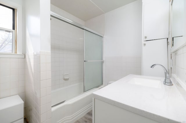 full bath featuring wainscoting, shower / bath combination with glass door, wood finished floors, vanity, and tile walls