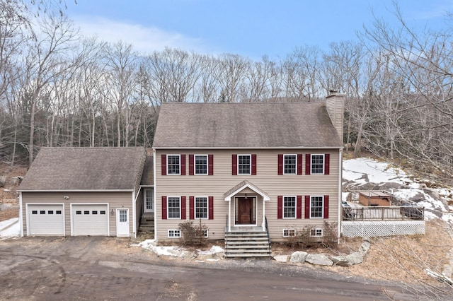 view of front facade featuring a garage, driveway, a shingled roof, and a chimney