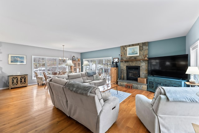living area with baseboards, a chandelier, a stone fireplace, and wood finished floors