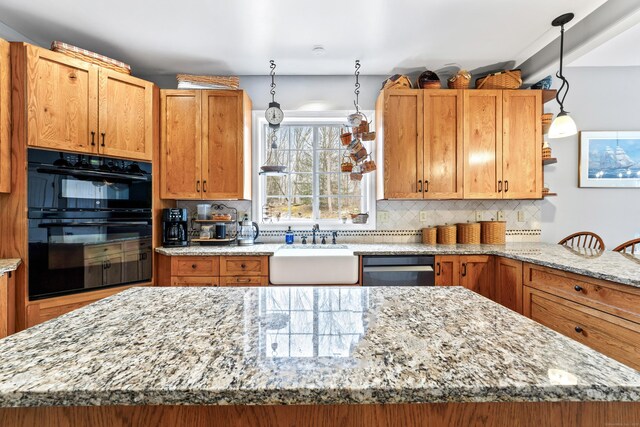 kitchen with dobule oven black, a sink, light stone countertops, and tasteful backsplash
