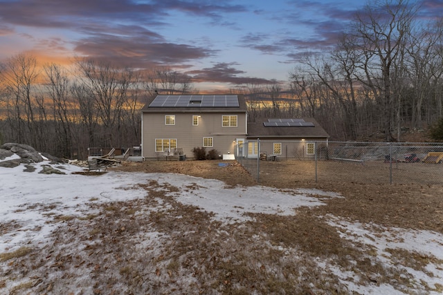 snow covered back of property featuring fence and solar panels