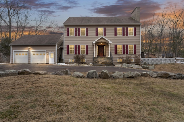 colonial inspired home with a shingled roof, a front lawn, a garage, a chimney, and driveway