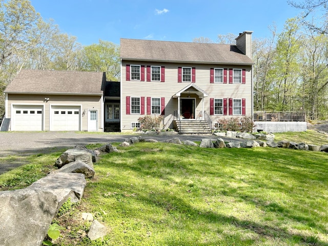 colonial-style house with aphalt driveway, a chimney, a front lawn, and a garage