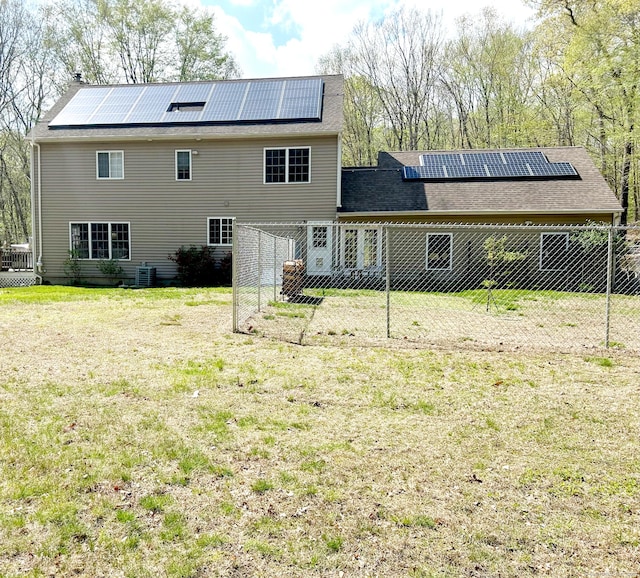 rear view of house featuring a lawn, roof mounted solar panels, and fence