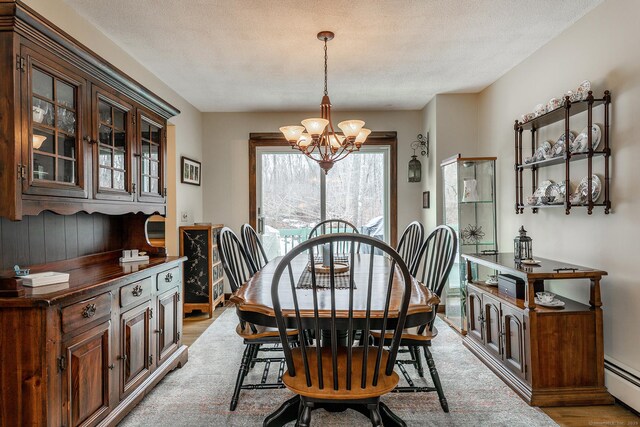 dining area with a baseboard heating unit, light wood-style floors, a textured ceiling, and an inviting chandelier