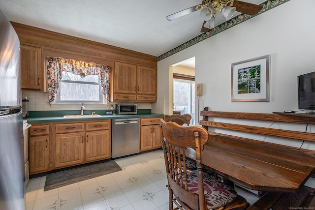 kitchen with a sink, appliances with stainless steel finishes, decorative backsplash, light floors, and brown cabinetry