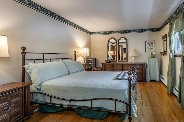 bedroom with baseboard heating and wood finished floors