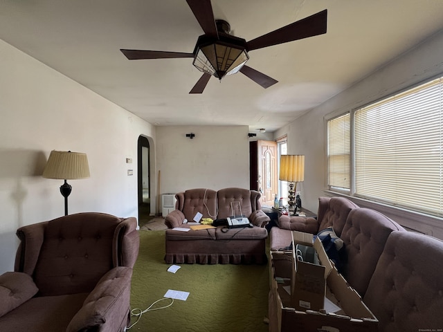 carpeted living room with ceiling fan and arched walkways