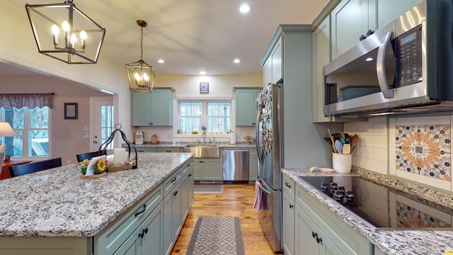 kitchen featuring stainless steel appliances, plenty of natural light, light wood-style flooring, and light stone countertops