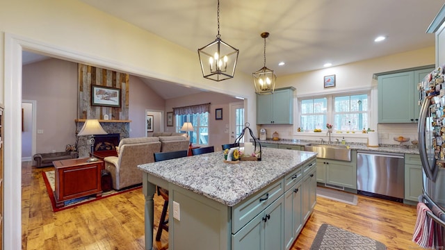 kitchen featuring a large fireplace, vaulted ceiling, stainless steel appliances, and light wood-style floors