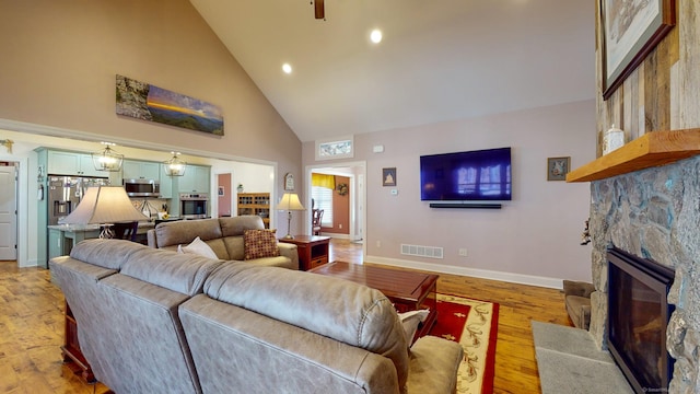 living area with high vaulted ceiling, light wood finished floors, a fireplace, and visible vents