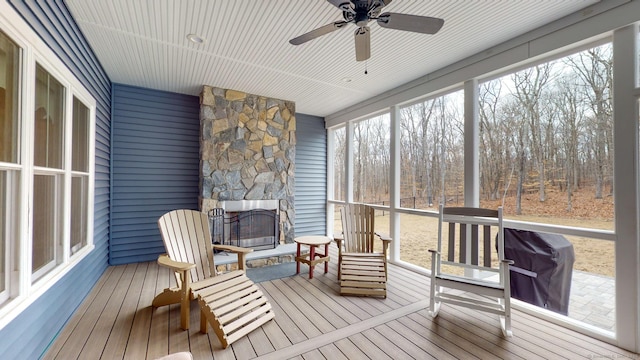 sunroom / solarium featuring a ceiling fan, an outdoor stone fireplace, and a healthy amount of sunlight