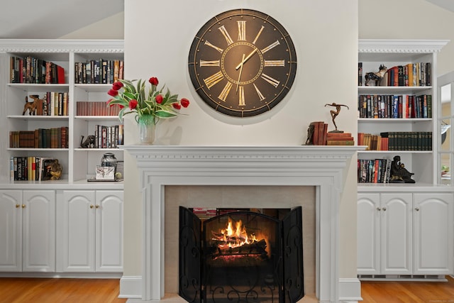 details with built in features, a warm lit fireplace, and wood finished floors