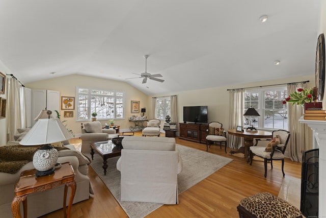 living area with vaulted ceiling, light wood-type flooring, a fireplace, and a ceiling fan