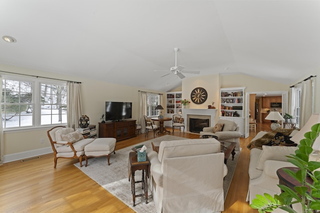 living area featuring a fireplace with flush hearth, plenty of natural light, visible vents, and light wood-style floors