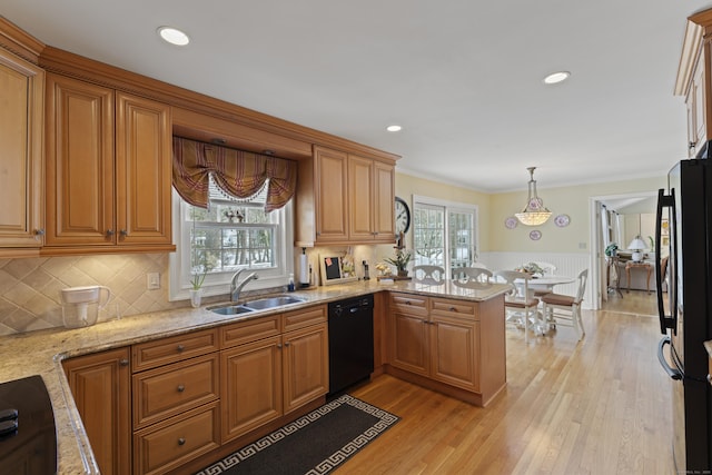 kitchen featuring wainscoting, a peninsula, a sink, black appliances, and a wealth of natural light