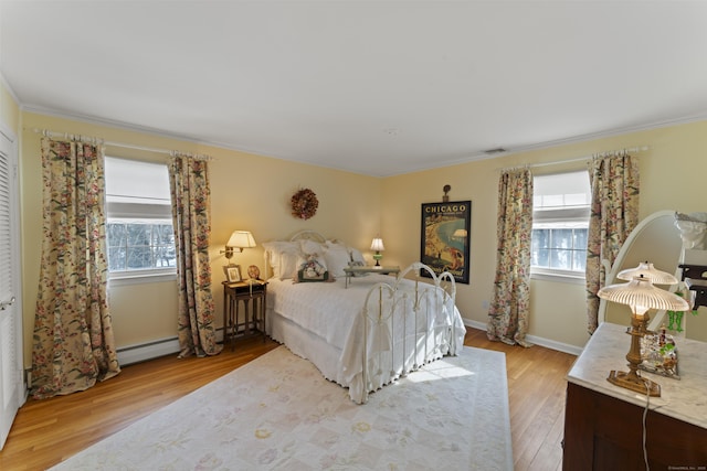 bedroom with a baseboard heating unit, light wood finished floors, multiple windows, and visible vents