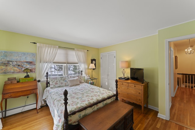 bedroom with a closet, an inviting chandelier, a baseboard heating unit, wood finished floors, and baseboards