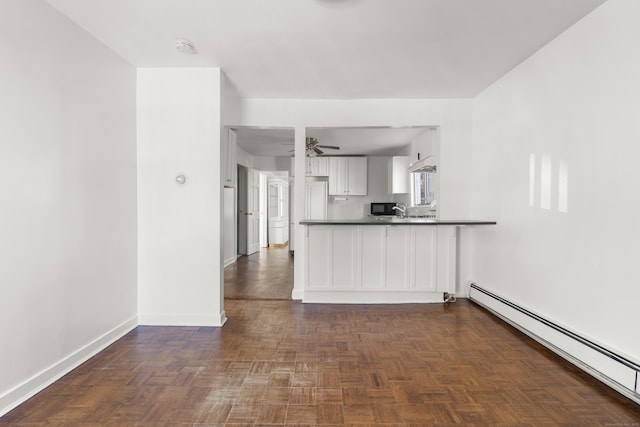 kitchen with dark countertops, baseboard heating, white cabinetry, ceiling fan, and baseboards