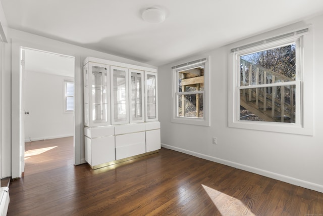 unfurnished bedroom featuring baseboard heating, baseboards, and dark wood finished floors