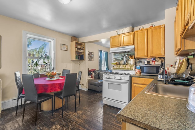 kitchen featuring white gas range oven, dark countertops, stainless steel microwave, dark wood-style flooring, and under cabinet range hood