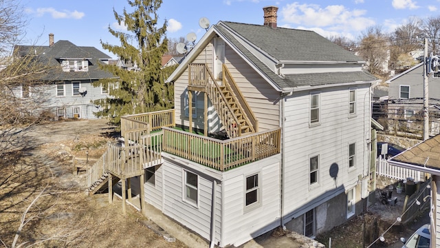 back of property with roof with shingles, a chimney, and stairs