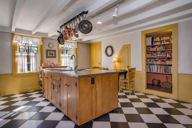 579 Taugwonk Rd, Stonington, CT 06378 - kitchen featuring dark floors, beamed ceiling, rail lighting, a kitchen island with sink, and brown cabinets