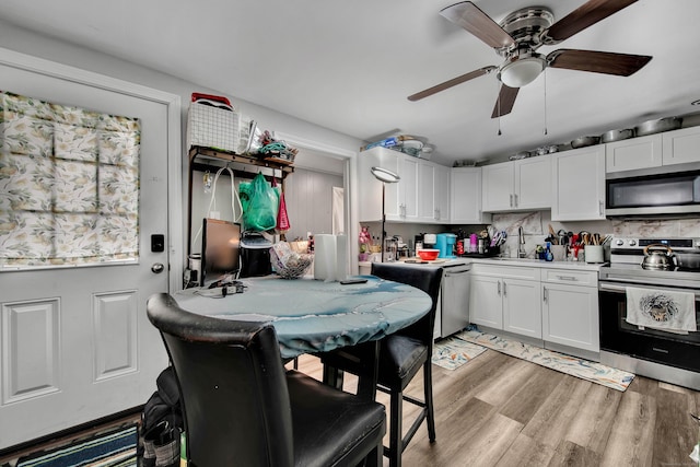 kitchen with stainless steel appliances, a sink, a ceiling fan, light wood-style floors, and white cabinets